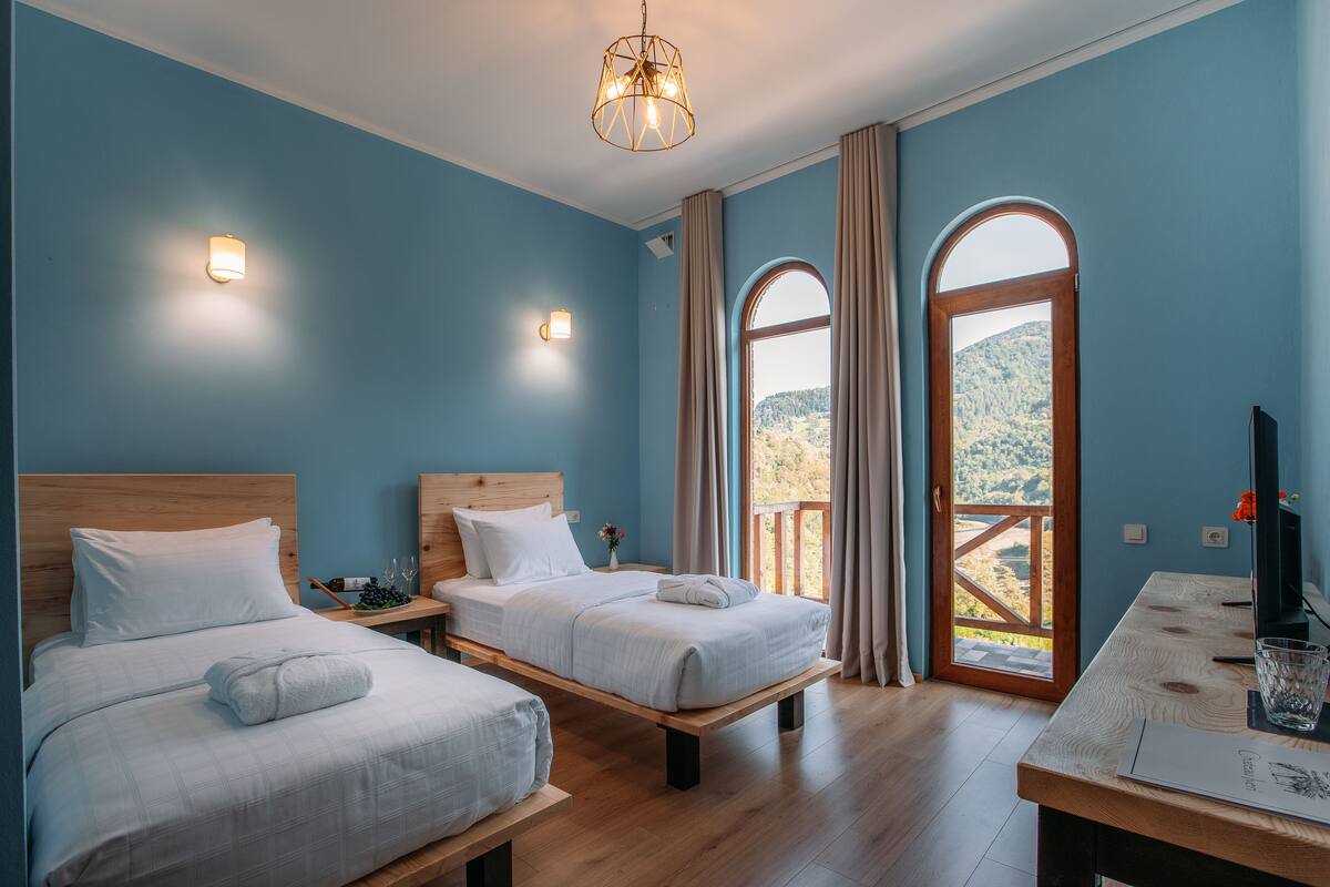 Une chambre avec deux lits, une table en bois et une grande fenêtre avec des rideaux.