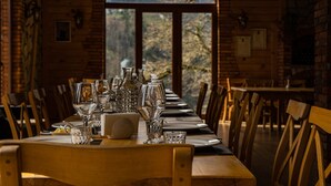 Una mesa de comedor de madera dispuesta con cristalería y platos, con vistas a árboles a través de un amplio ventanal.