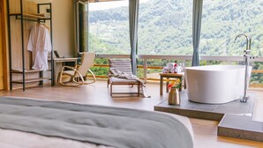 Un dormitorio con una cama grande, un escritorio con una computadora portátil, una silla, una bañera y vistas a un paisaje montañoso.
