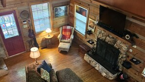 Ein gemütliches Blockhaus-Interieur mit Holzboden, Kamin, Sofa, Sessel und Fernseher.