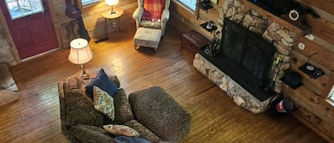 L’intérieur d’un chalet accueillant, avec un plancher en bois, une cheminée, un canapé, un fauteuil et un téléviseur.