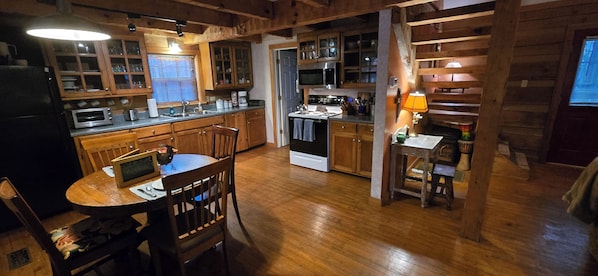 Una cocina con armarios de madera, una mesa de comedor, sillas, una estufa y un microondas.