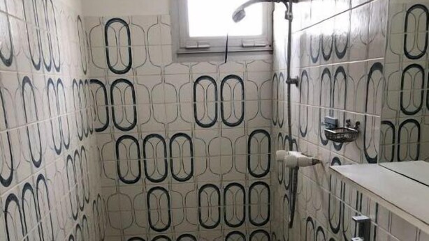 A bathroom with a patterned tile wall, a white sink, and a window above the mirror.