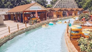 Ein Wasserpark mit Achterbahn, Schwimmbecken und aufblasbaren Ringen sowie einem Gebäude mit der Aufschrift 'LOCKERS'.