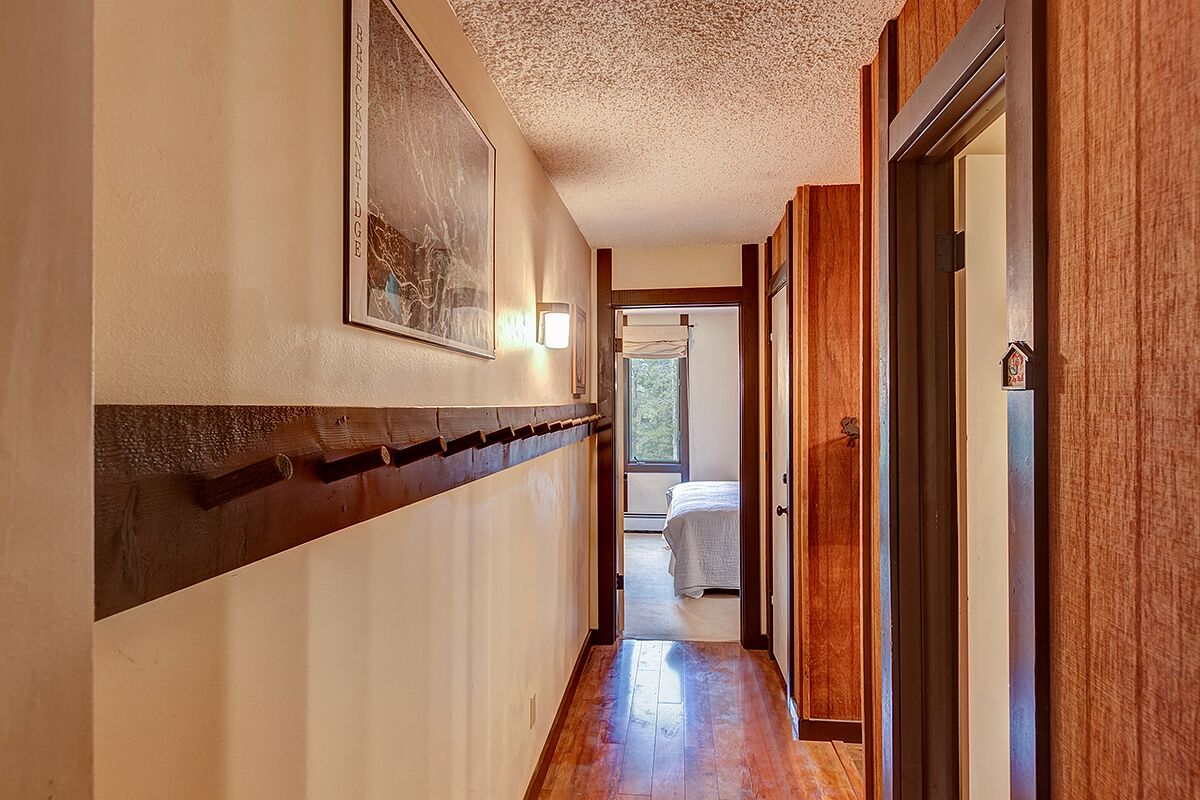A narrow hallway with wooden flooring, a framed picture on the wall, and a door leading to a bedroom with a bed.