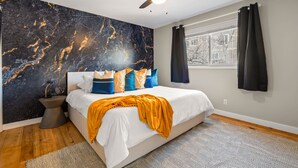 Une chambre à coucher avec un lit, un ventilateur de plafond, une fenêtre avec des rideaux et un mur décoré d’un motif imitant le marbre.