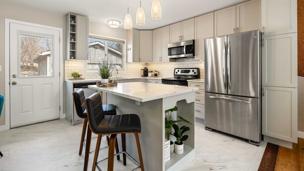 Une cuisine moderne dotée d’un îlot central, d’appareils électroménagers en acier inoxydable et de luminaires suspendus.