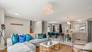 Un salon moderne avec un canapé d’angle gris, une table basse et un coin repas, la cuisine étant visible au fond.