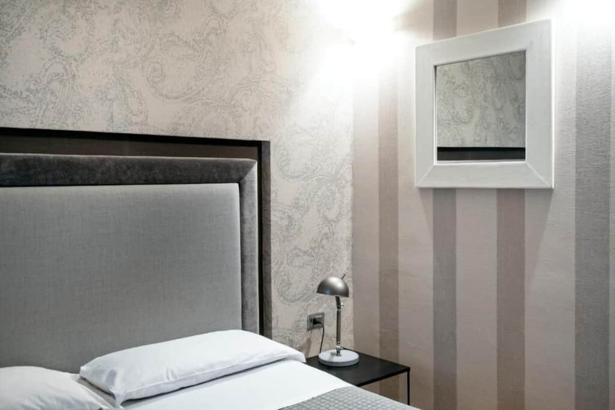 A neatly made bed with white bedding, a small bedside table with a lamp, and a framed picture on the wall.