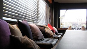 A row of leather sofas with various colored cushions, a table with a white tablecloth, and a window with blinds. - HOTEL SALUS (Pescara)
