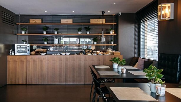 A modern restaurant with a wooden counter, shelves with plants, and a seating area with tables and chairs. - HOTEL SALUS (Pescara)