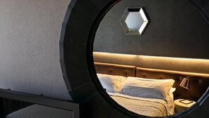A circular room with a bed, a nightstand, and a hexagonal mirror on the wall. - HOTEL SALUS (Pescara)