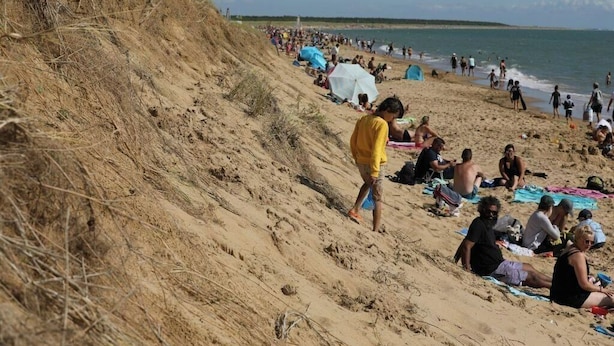 Ein sandiger Strand mit Personen, die sich sonnen und am Ufer entlang spazieren.