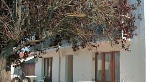 Ein Gebäude mit einer Terrassenfläche, komplett mit Tisch und Stühlen, einem kleinen Garten und einem Baum.