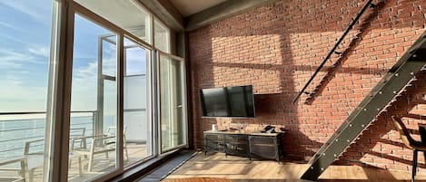 Ein Zimmer mit einem großen Fenster, einer Holzbank, einem an einer Ziegelwand montierten Fernseher und einer Treppe.
