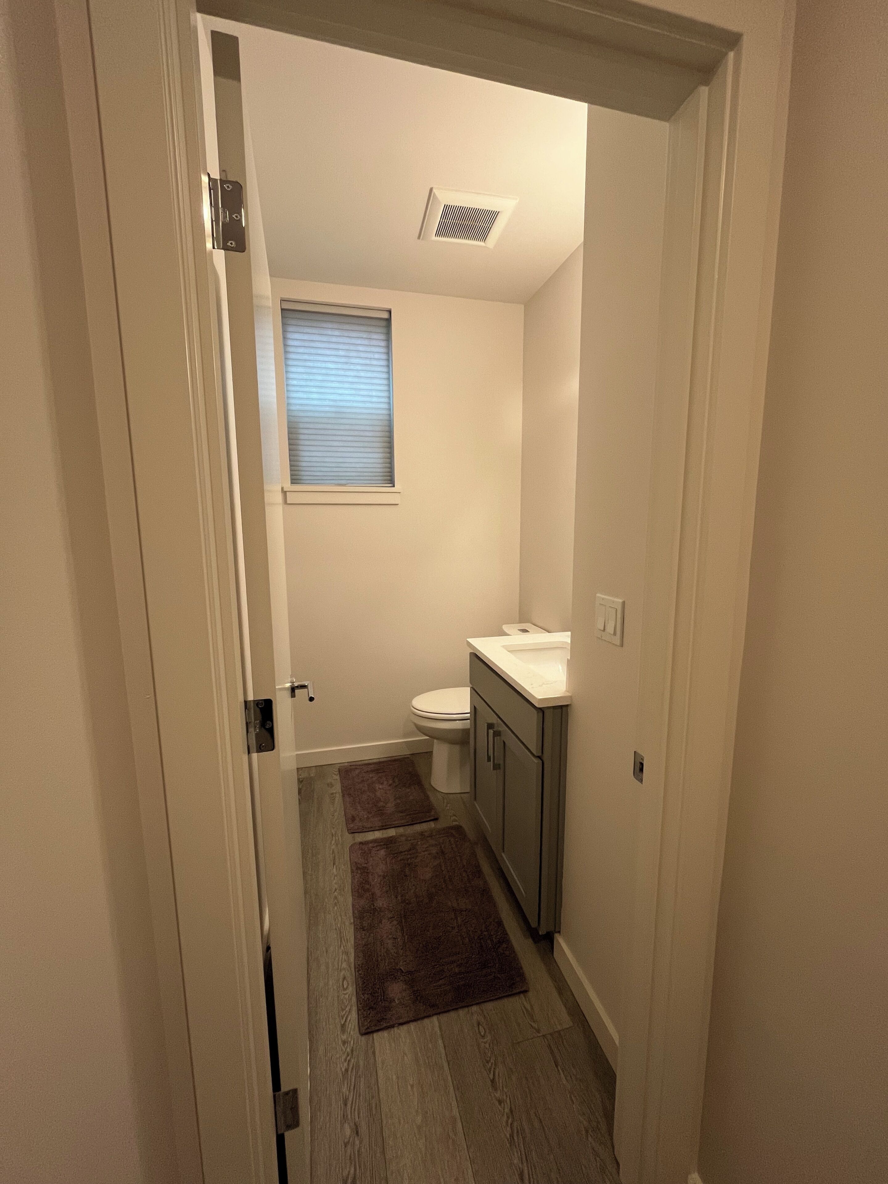 Een smalle gang die leidt naar een badkamer met toilet, wastafel en raam.