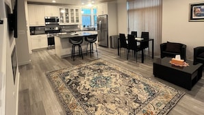 A modern kitchen with white cabinets, a dining area with black chairs, and a large rug. - Bright Townhome in Trendy Ballard (Seattle)