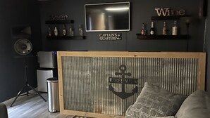 Uma sala de estar moderna com um sofá, uma TV na parede e prateleiras com garrafas.