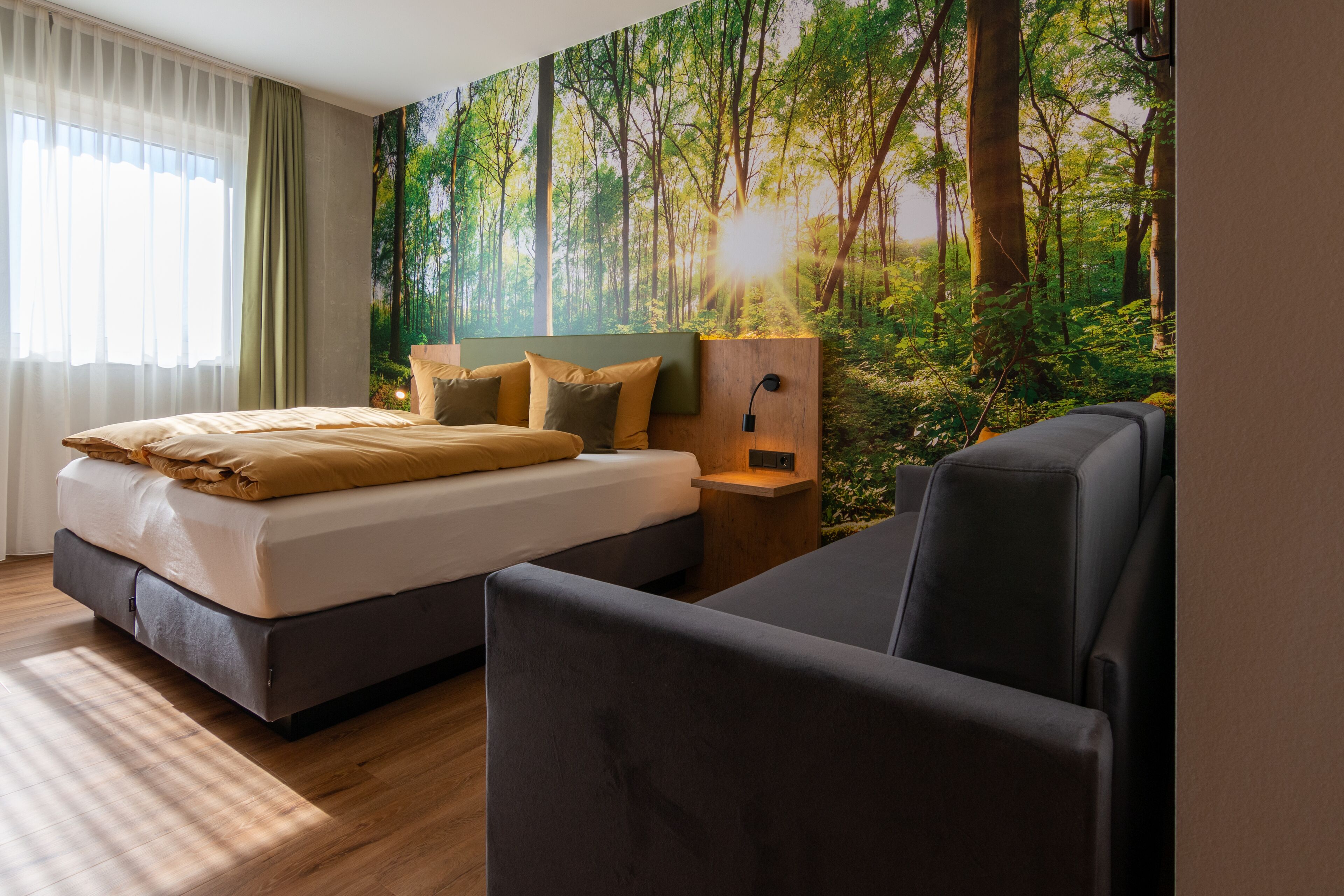 Un dormitorio con cama, mesita de noche, lámpara de pared y un mural grande con un bosque.