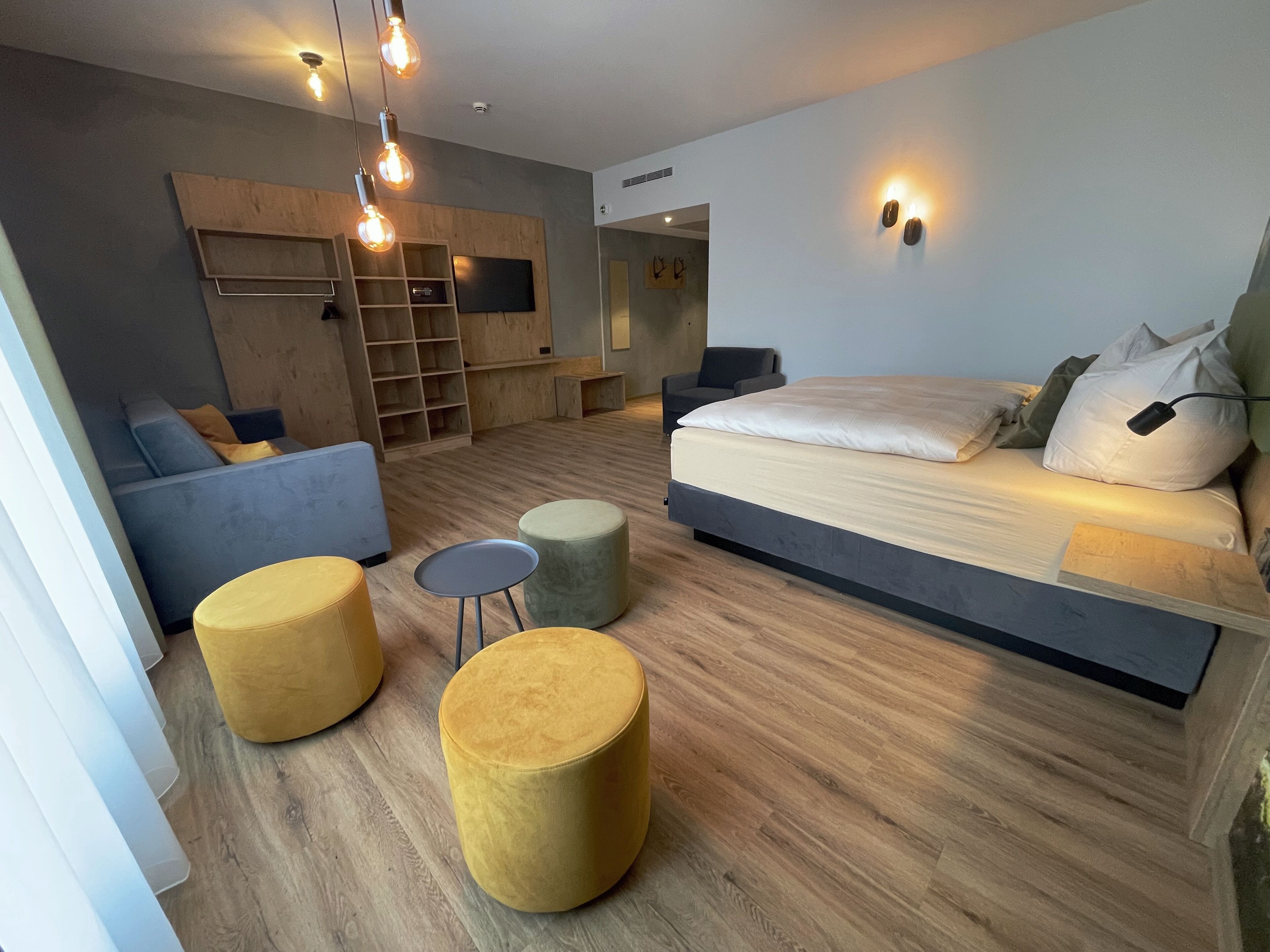 Quarto moderno com cama, dois pufes, sofá, televisão e estantes embutidas.