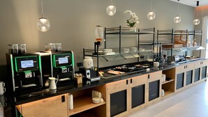 Hotellin buffetissa on itsepalveluun tarkoitetut kahviautomaatit, monipuolinen ruokavalikoima ja lasivitriini.