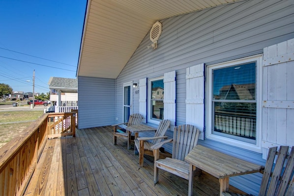 A wooden deck with two Adirondack chairs and a small table, overlooking a street with houses.
