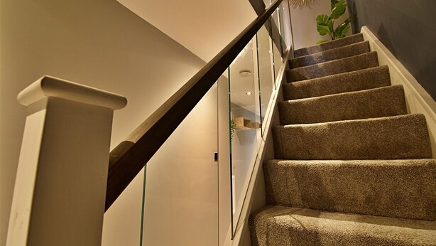 A staircase with carpeted steps and a wooden handrail, leading to a landing with a glass railing. - Bellerose 2 (Lancaster)