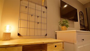A wooden desk with drawers, a pegboard wall, a flat-screen TV, and a potted plant. - Bellerose 2 (Lancaster)