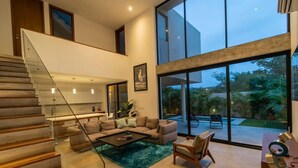 A modern living room with a staircase, a large window, and a view of the outdoors.