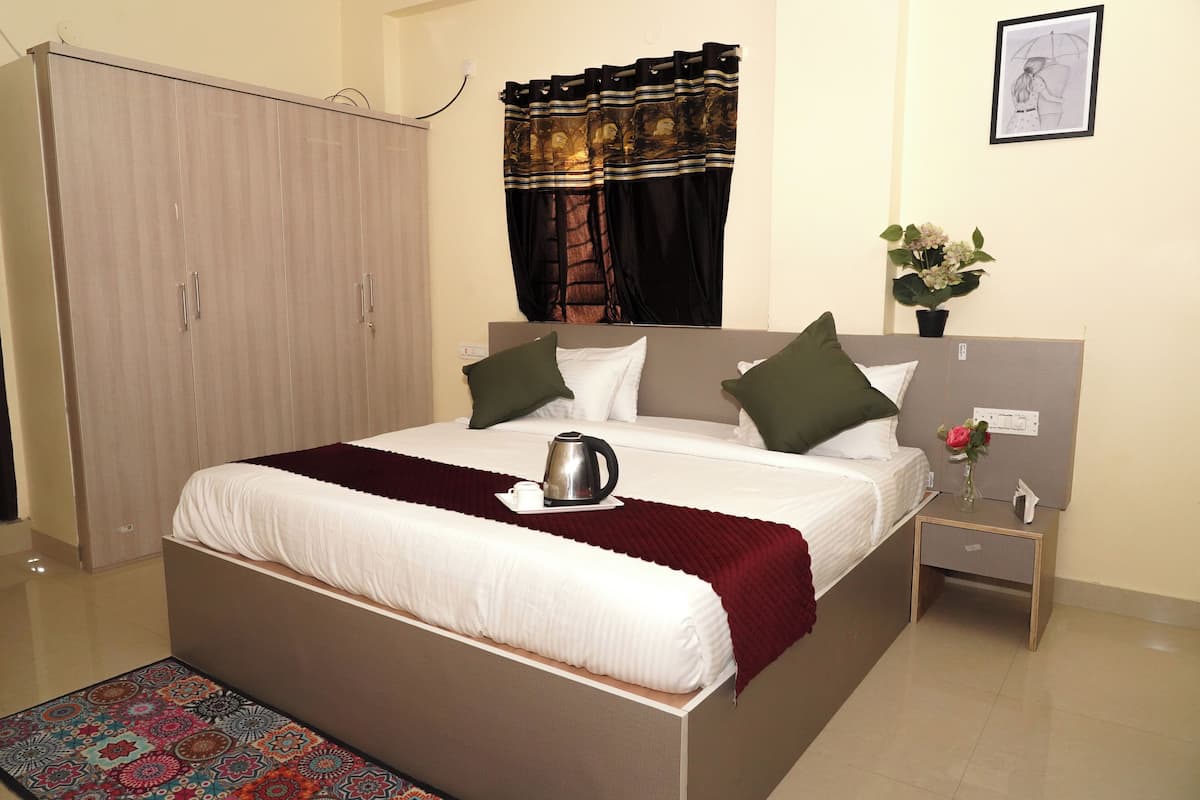 A neatly made bed with a white comforter, two pillows, and a red throw blanket. A small bedside table with a vase of flowers is visible.