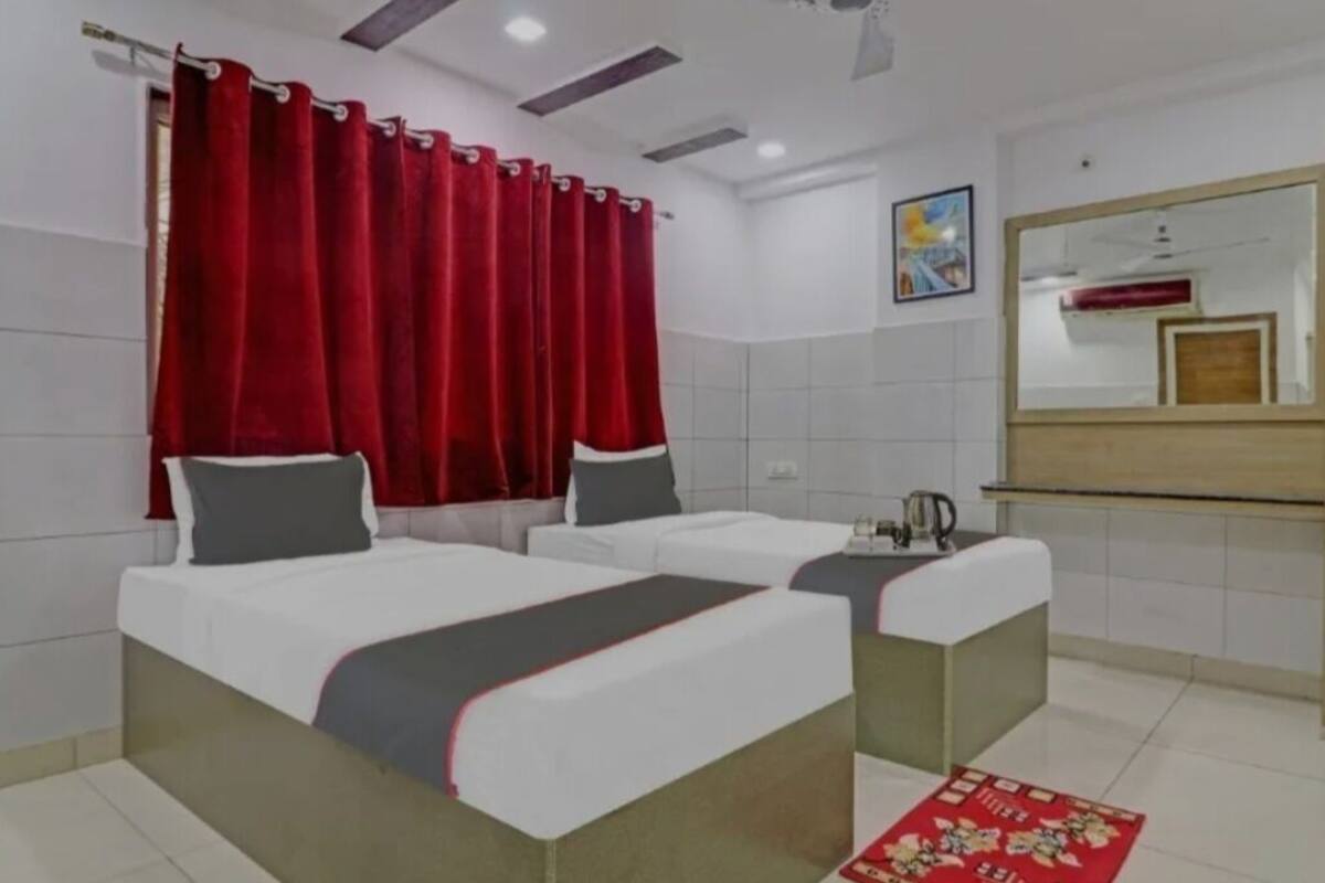 A hotel room with two beds, a red curtain, a mirror, and a small table.