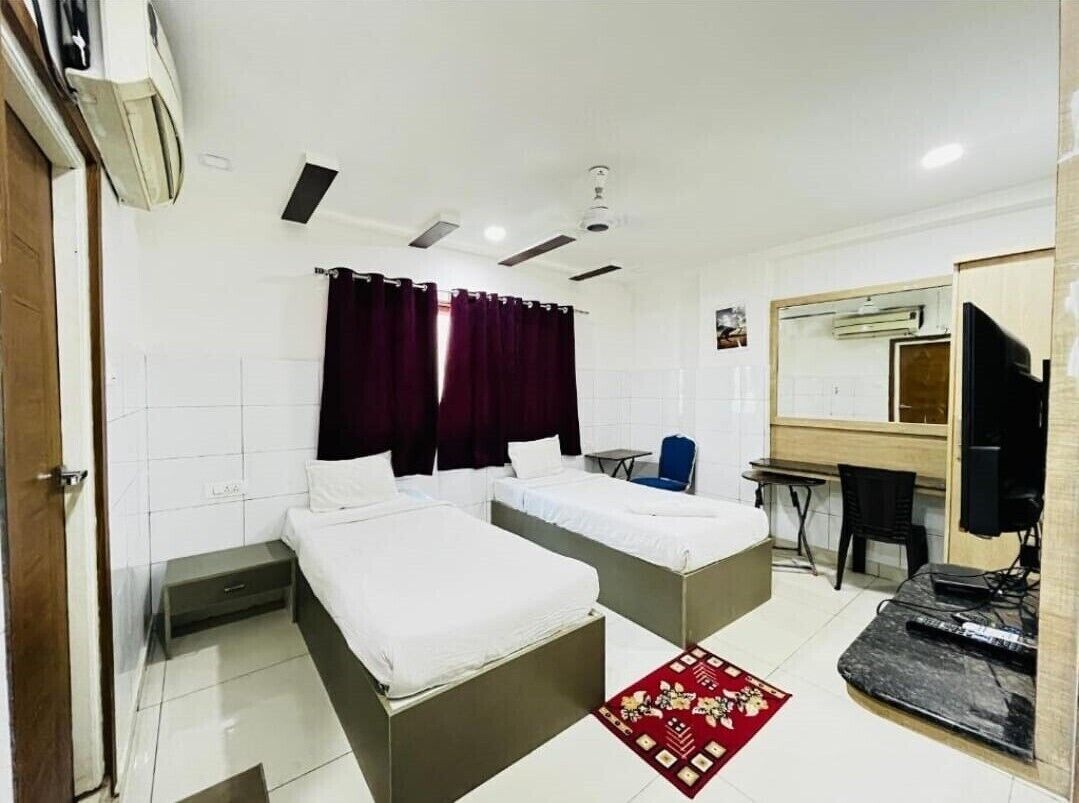 A hotel room with two beds, a desk, a chair, a TV, and a mirror.