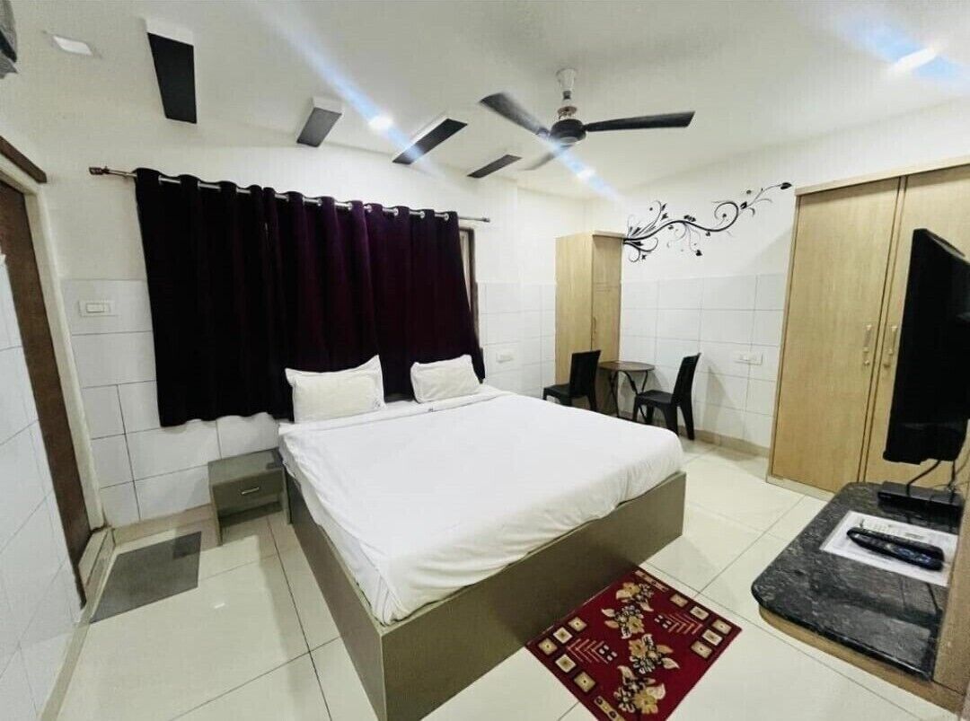 A bedroom with a bed, a desk, a chair, a TV, and a ceiling fan.