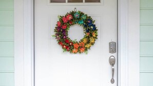 A white door with a colorful floral wreath and a doorbell.