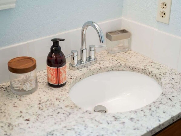 A bathroom sink with a granite countertop, a soap dispenser, and a glass jar with a wooden lid. - 4BR Game-Day Retreat - Foosball & Fire Pit (Fayetteville)