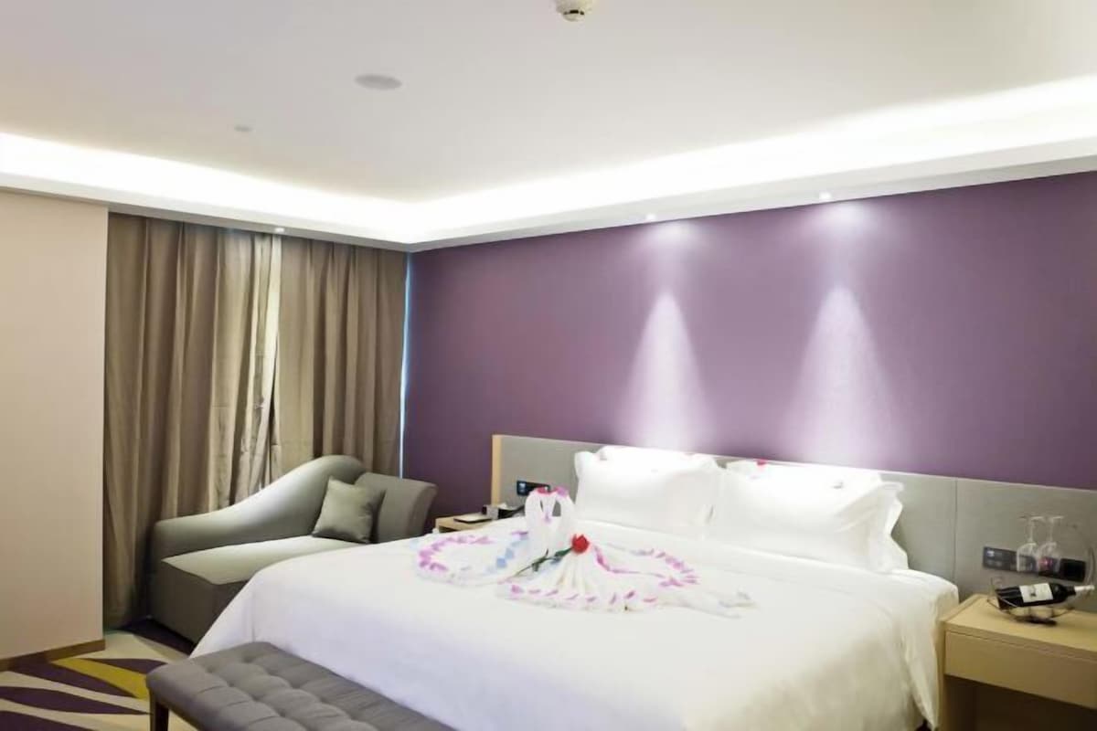 A hotel room with a bed, a chair, a bedside table, and a window with curtains.