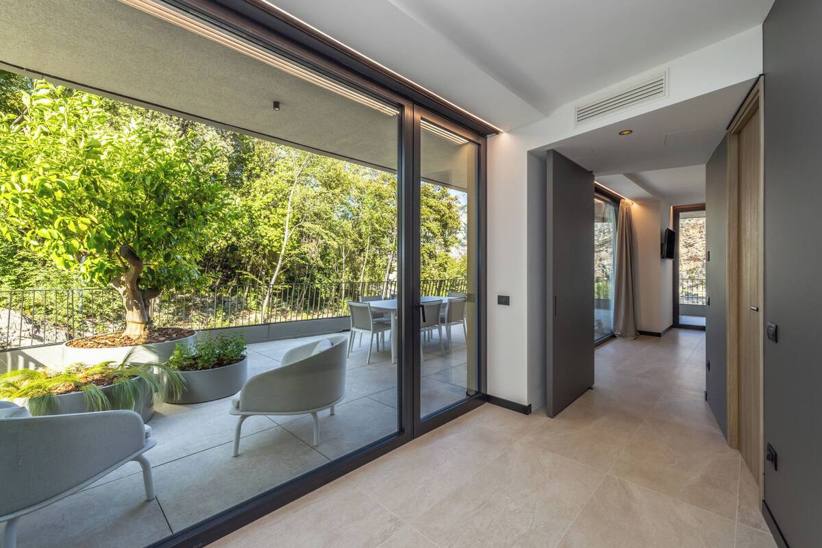 Un intérieur moderne avec une porte vitrée donnant sur un patio extérieur aménagé avec des sièges et un arbre.