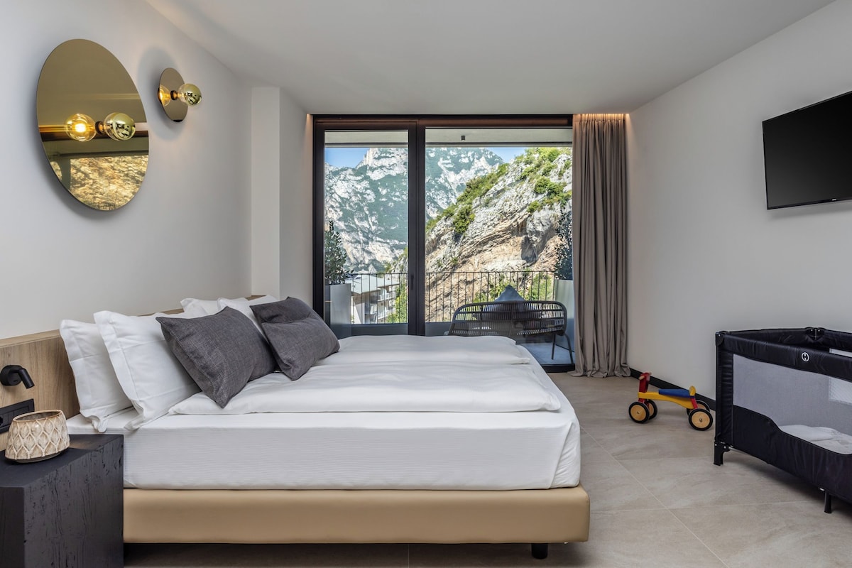A modern bedroom with a large bed, a TV, a balcony with a view of mountains, and a child's play area.