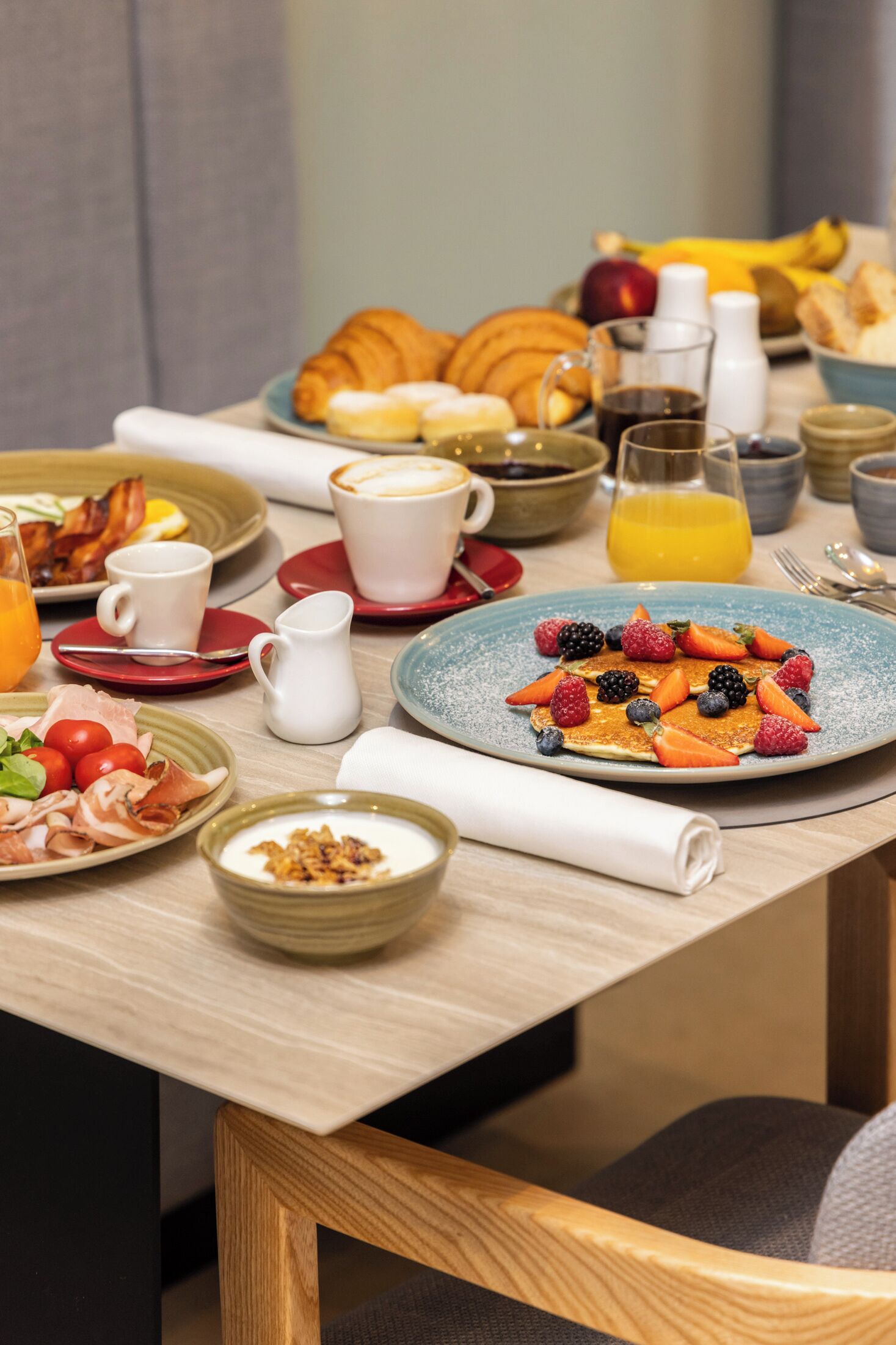 A breakfast table with various dishes, including pancakes with berries, croissants, and a glass of orange juice.