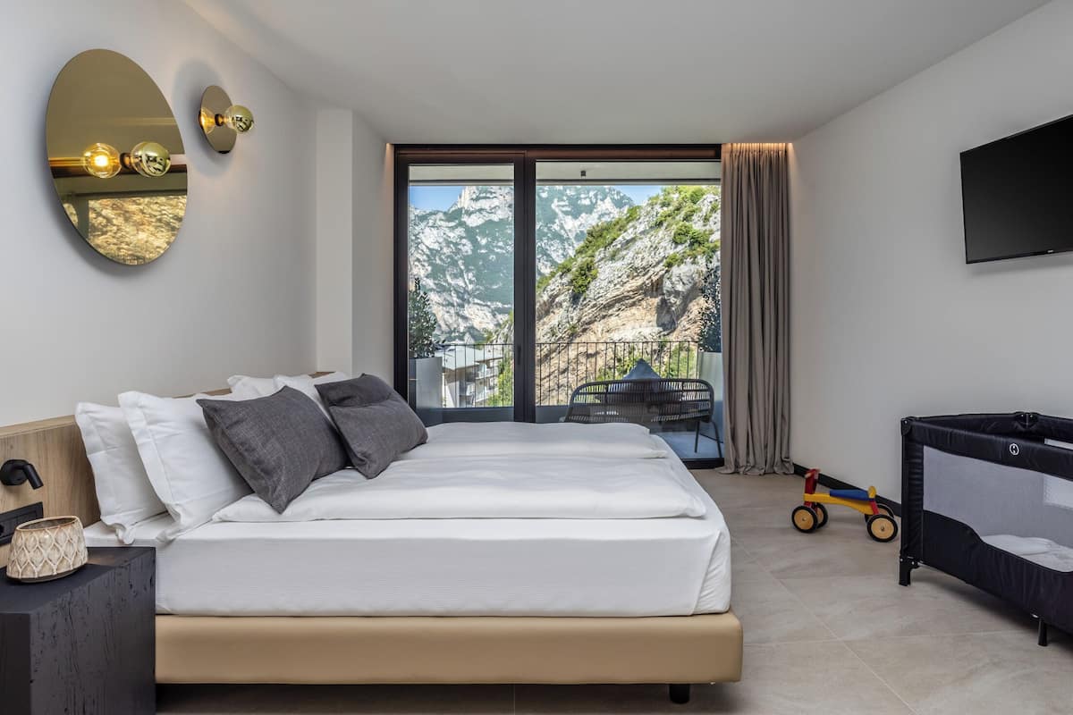 Une chambre moderne avec un grand lit, une télévision, un balcon offrant une vue sur les montagnes et un espace de jeux pour enfants.