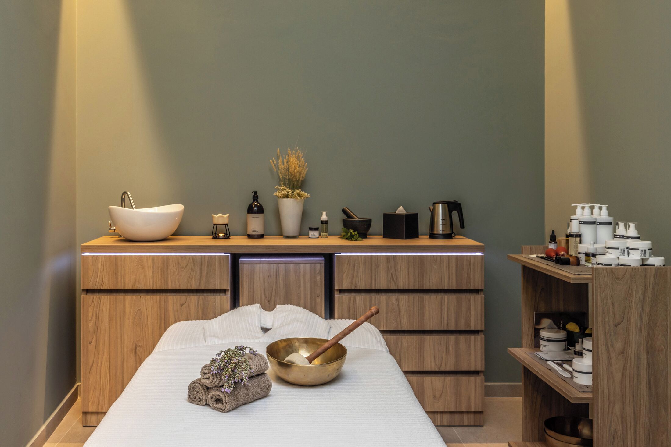 Una spa con un mobile da toeletta in legno, un ampio lavabo bianco, una ciotola con un cucchiaio di legno e diversi articoli da toilette.