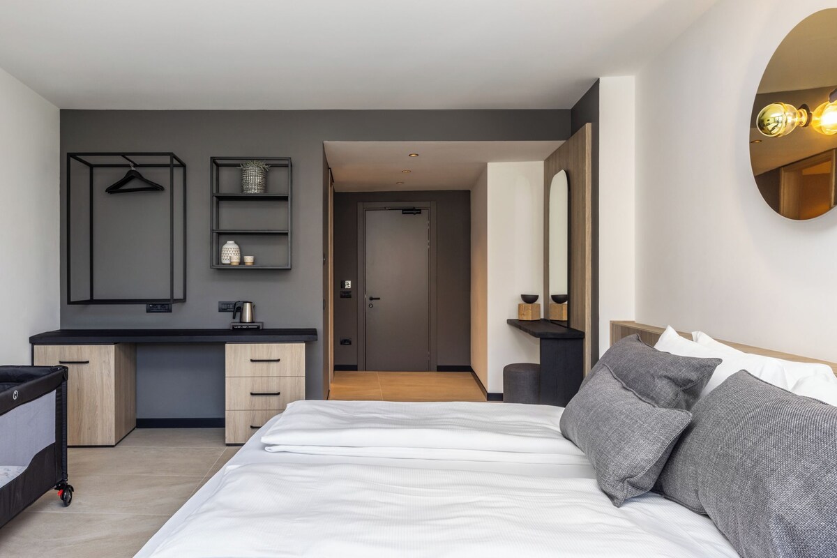 A modern hotel room with a bed, bedside tables, a desk, and a wardrobe.