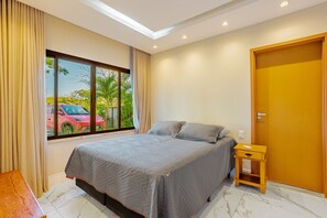 Un dormitorio con cama, mesita de noche, puerta de madera y ventana con cortinas.