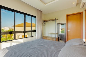 Habitación de hotel con una cama grande, un armario, un espejo y una ventana con vistas a edificios y zonas verdes.