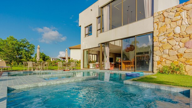 Et moderne hus med swimmingpool, udendørs siddepladser og en stenvæg.