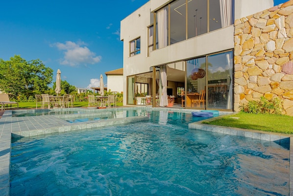 A modern house with a swimming pool, outdoor seating, and a stone wall.