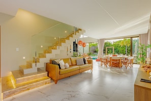 Ein modernes Wohnzimmer mit einer Couch, einem Essbereich mit Tisch und Stühlen sowie einer Treppe mit Glastrennläufern.