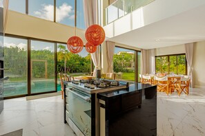 A modern kitchen with a large island, large windows, and a view of a pool and garden.