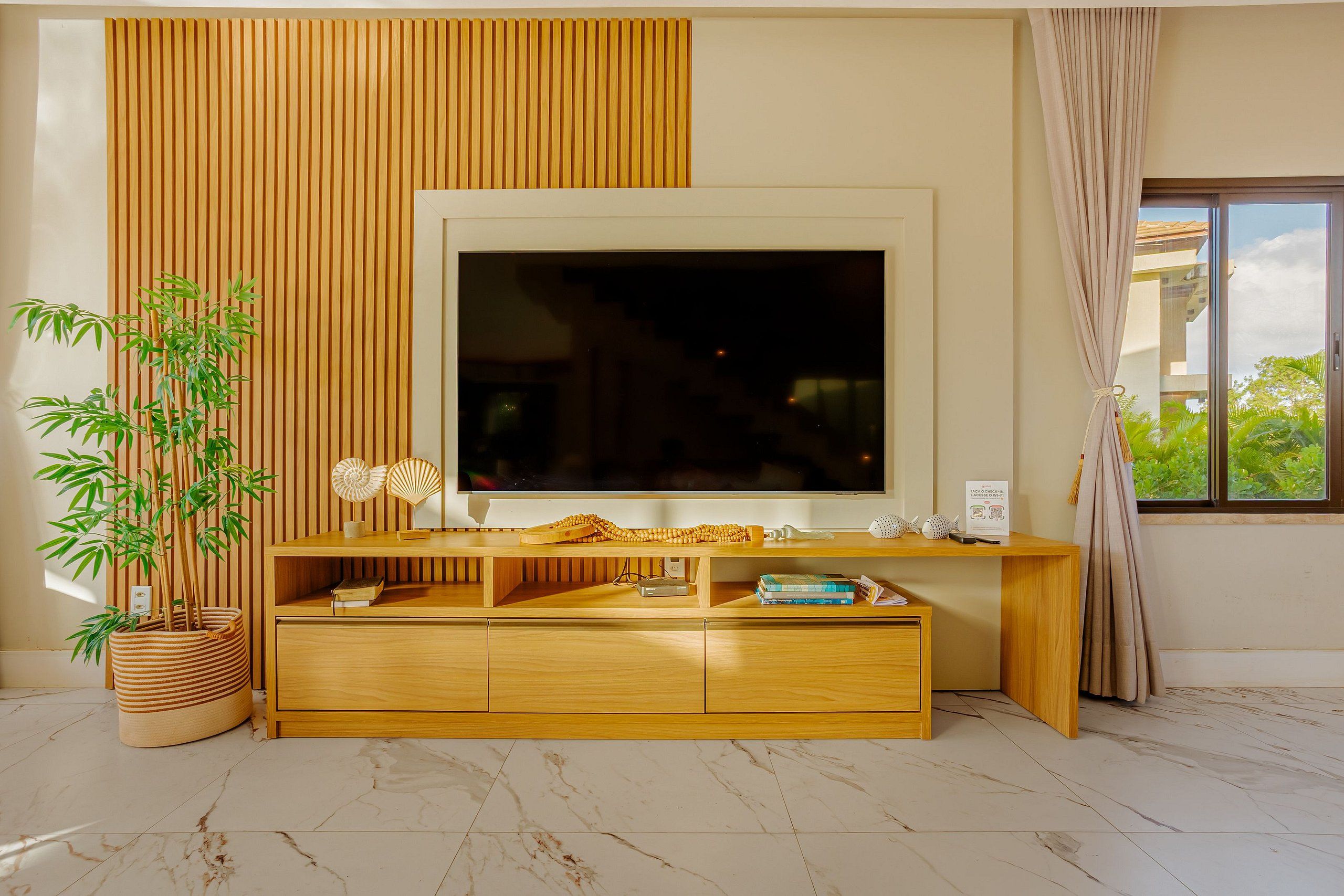 Una sala de estar moderna con un televisor de pantalla plana grande, un mueble de entretenimiento de madera y una planta de bambú en maceta.