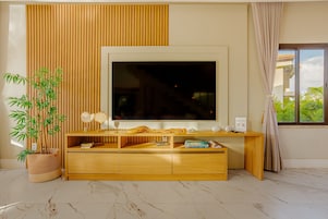 Una sala de estar moderna con un televisor de pantalla plana grande, un mueble de entretenimiento de madera y una planta de bambú en maceta.